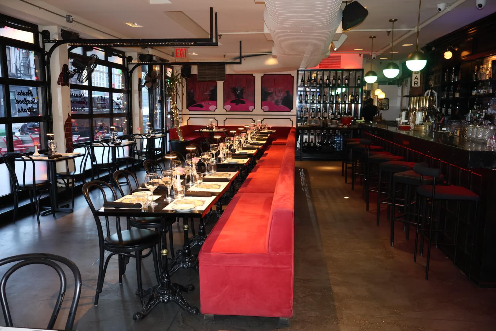Long row of black tables and chairs placed against red booth with full bar on the right