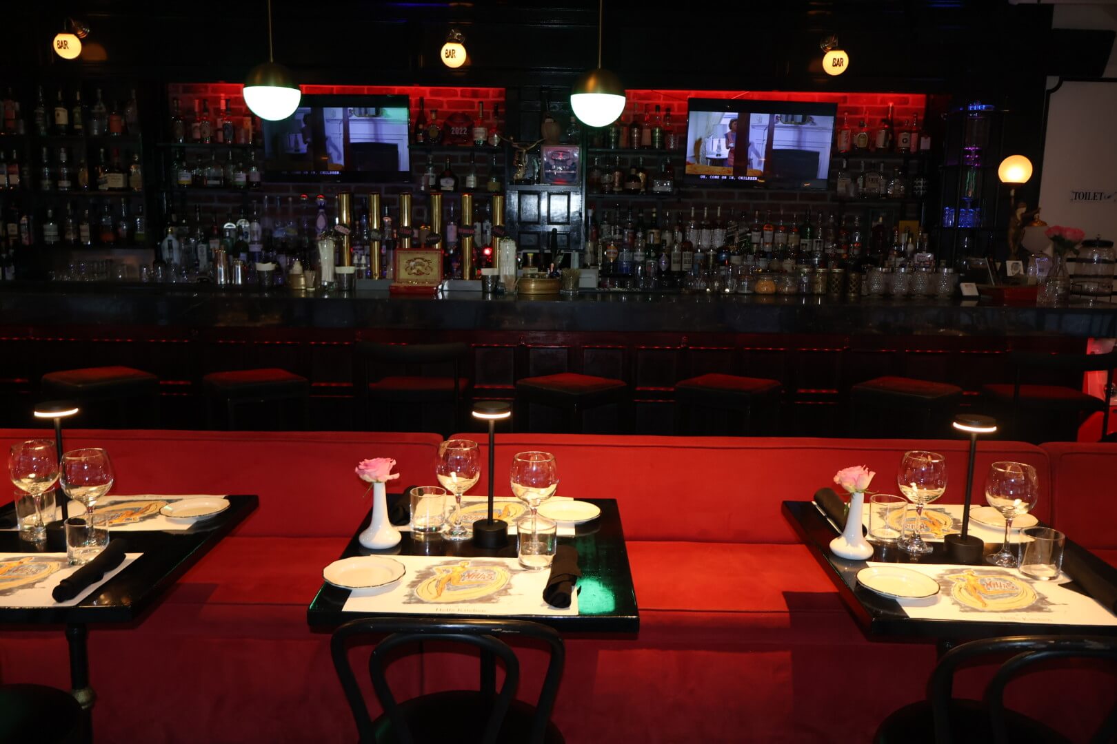 Three black tables and chairs against a red booth with fully stocked bar behind
