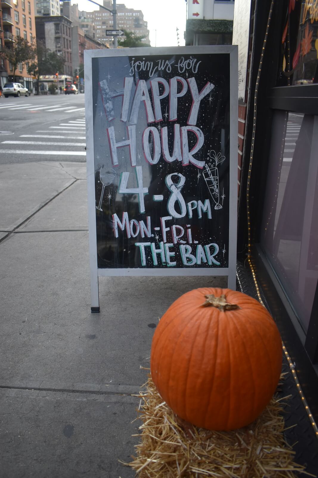 Sidewalk sign that says 'Happy Hour 4-8pm Mon-Fri' with a pumpkin in front of it