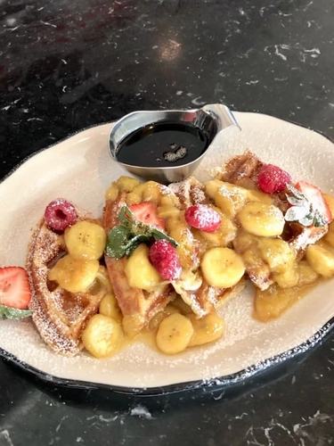 Brunch waffles topped with bananas, respberries, strawberries and powdered sugar and a side of syrup