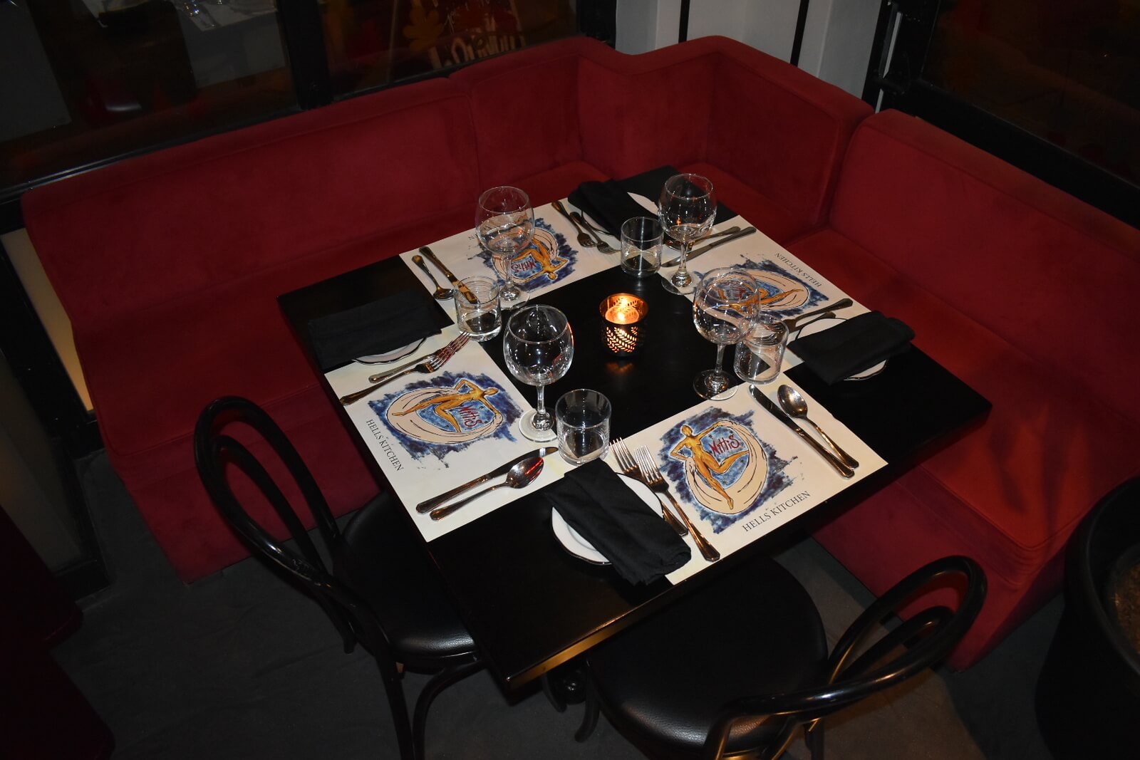 Black table in a corner booth set for four with 2 black chairs